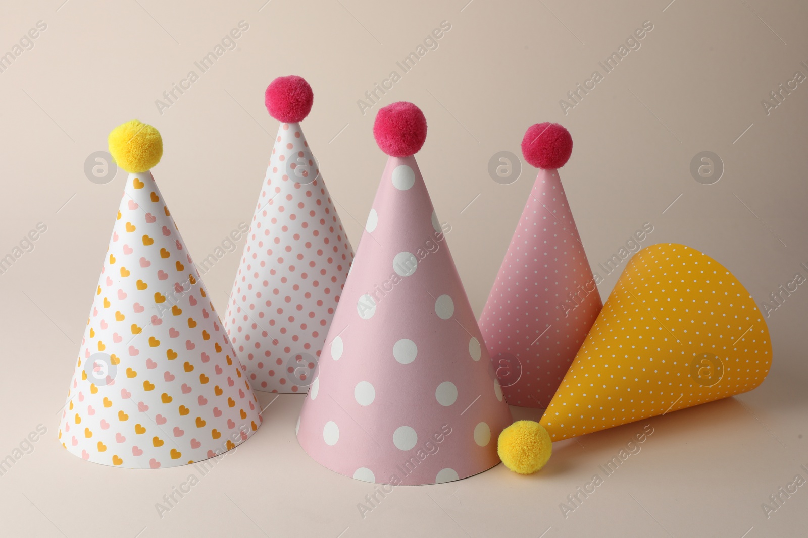 Photo of Beautiful party hats with pompoms on beige background