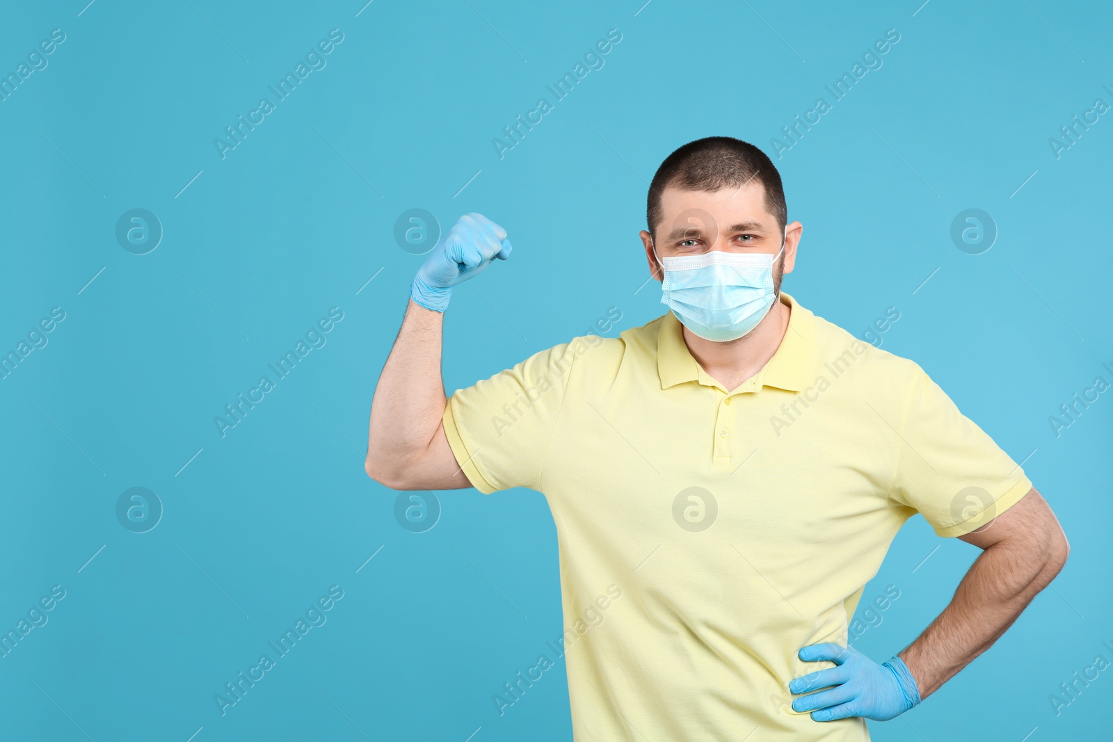 Photo of Man with protective mask and gloves showing muscles on light blue background, space for text. Strong immunity concept