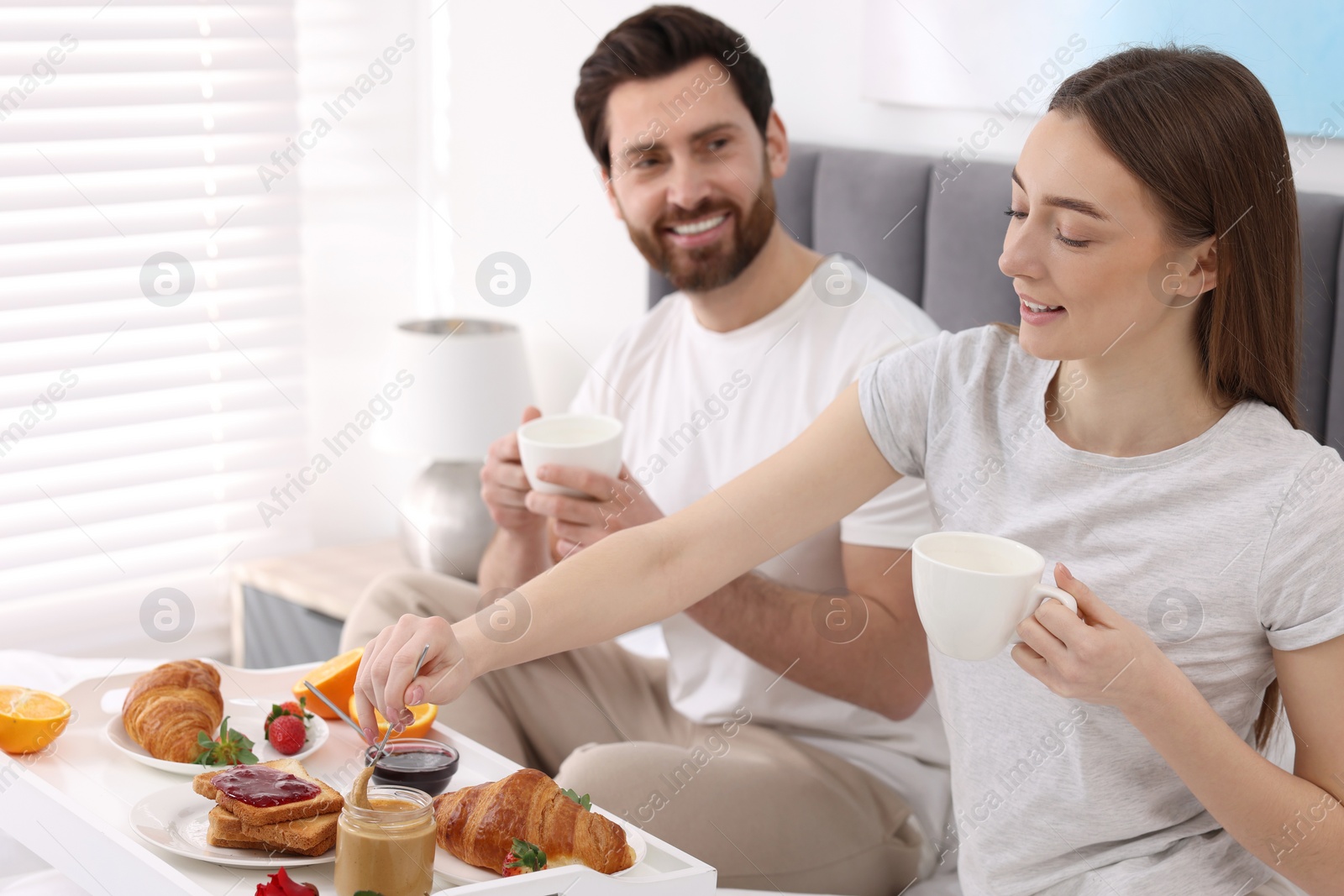 Photo of Happy couple eating tasty breakfast on bed at home