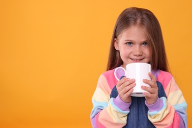 Photo of Happy girl with white ceramic mug on orange background, space for text