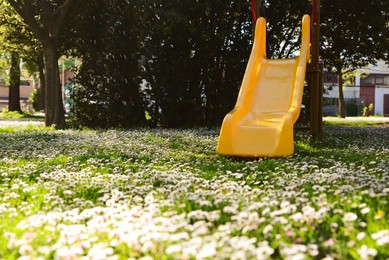 Photo of Yellow children's slide and beautiful flowers in park on sunny day
