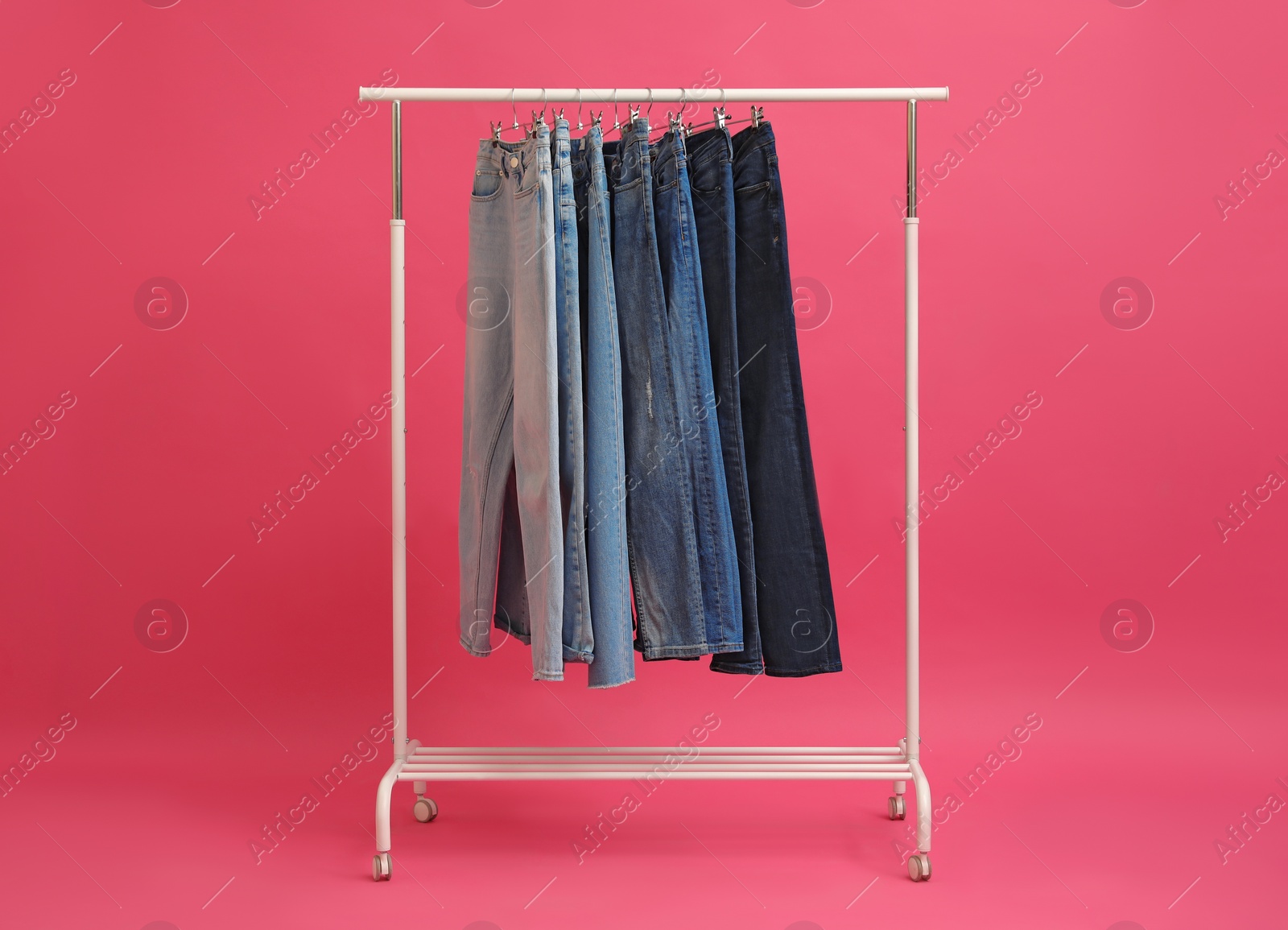 Photo of Rack with stylish jeans on pink background