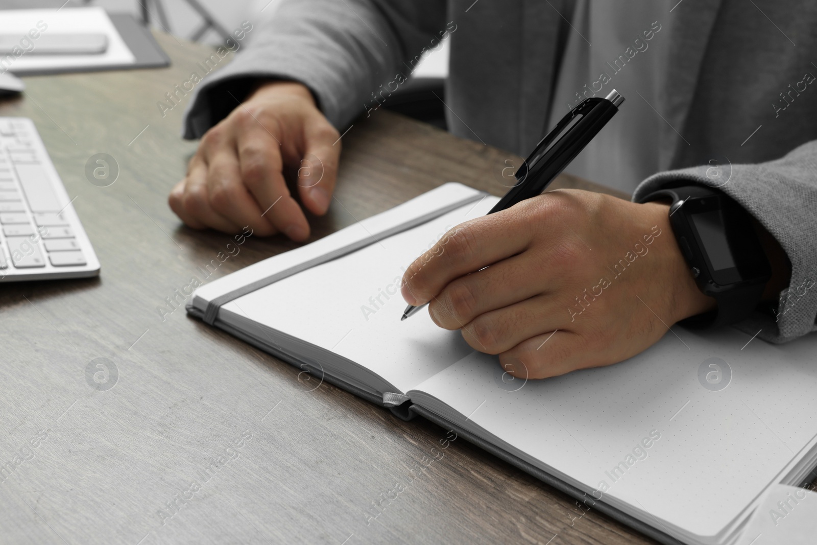 Photo of Boss writing in notebook at wooden table, closeup