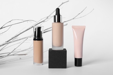 Photo of Bottles and tube of skin foundation with decorative twigs on white background. Makeup product