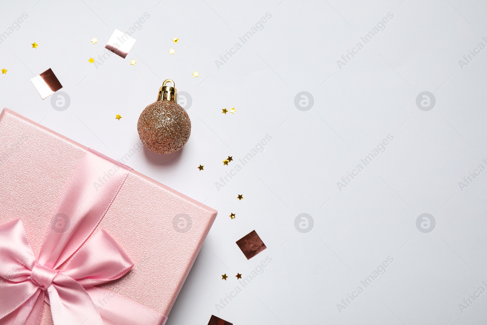 Photo of Pink gift box, Christmas ball and confetti on white background, flat lay. Space for text