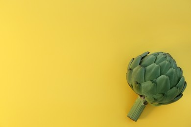 Photo of Whole fresh raw artichoke on yellow background, top view. Space for text