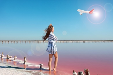 Image of Beautiful woman near pink lake and airplane in sky on background. Summer vacation