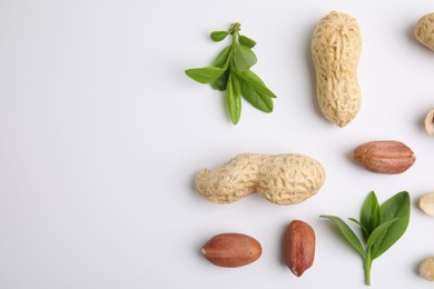 Fresh peanuts and leaves on white table, flat lay. Space for text