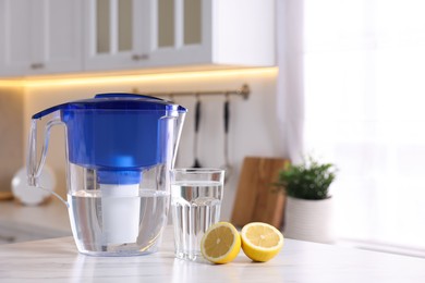 Water filter jug, glass and lemon on white marble table in kitchen, closeup. Space for text