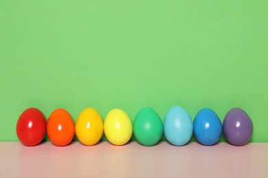 Photo of Easter eggs on pink wooden table against green background, space for text