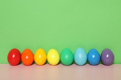 Easter eggs on pink wooden table against green background, space for text