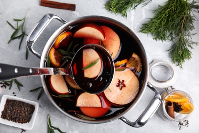 Photo of Ladle with delicious mulled wine over cooking pot on grey marble, flat lay
