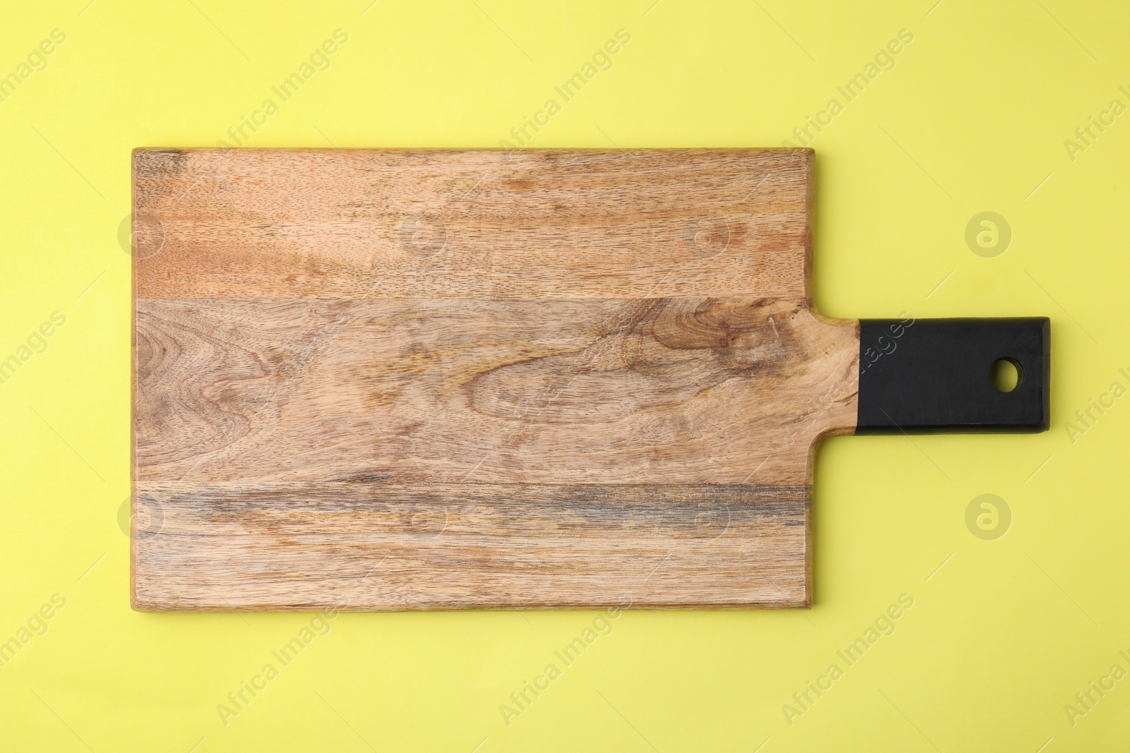 Photo of One wooden cutting board on yellow background, top view. Cooking utensil