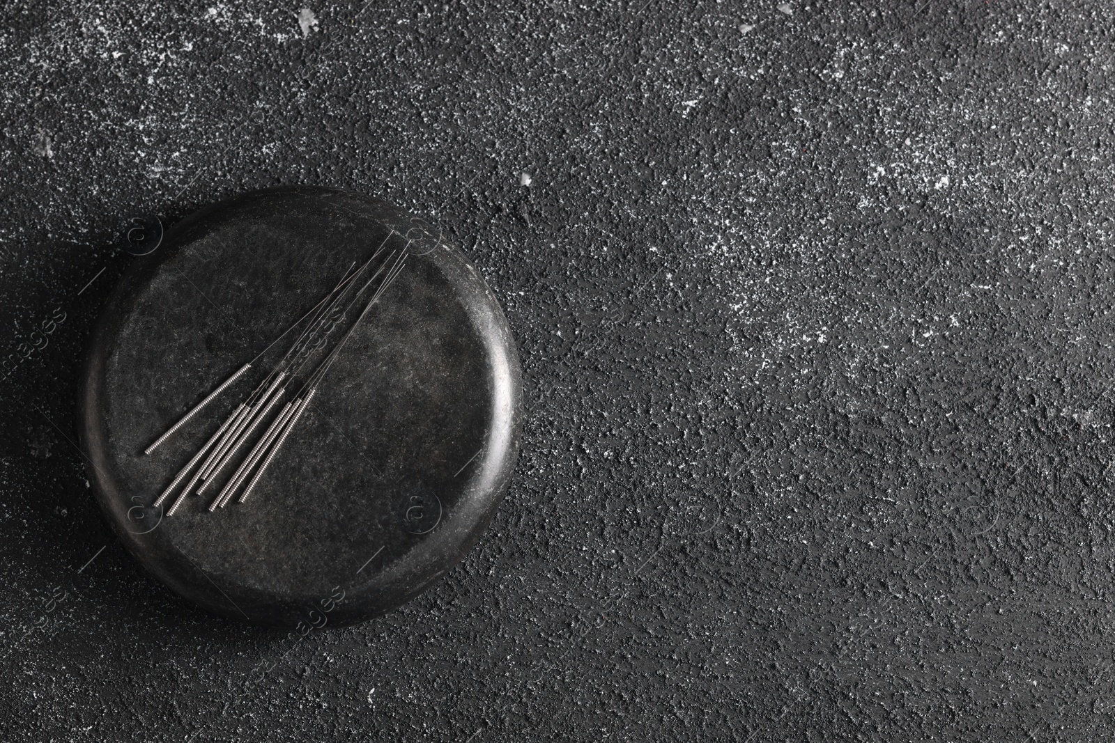 Photo of Acupuncture needles and spa stone on black textured table, top view. Space for text