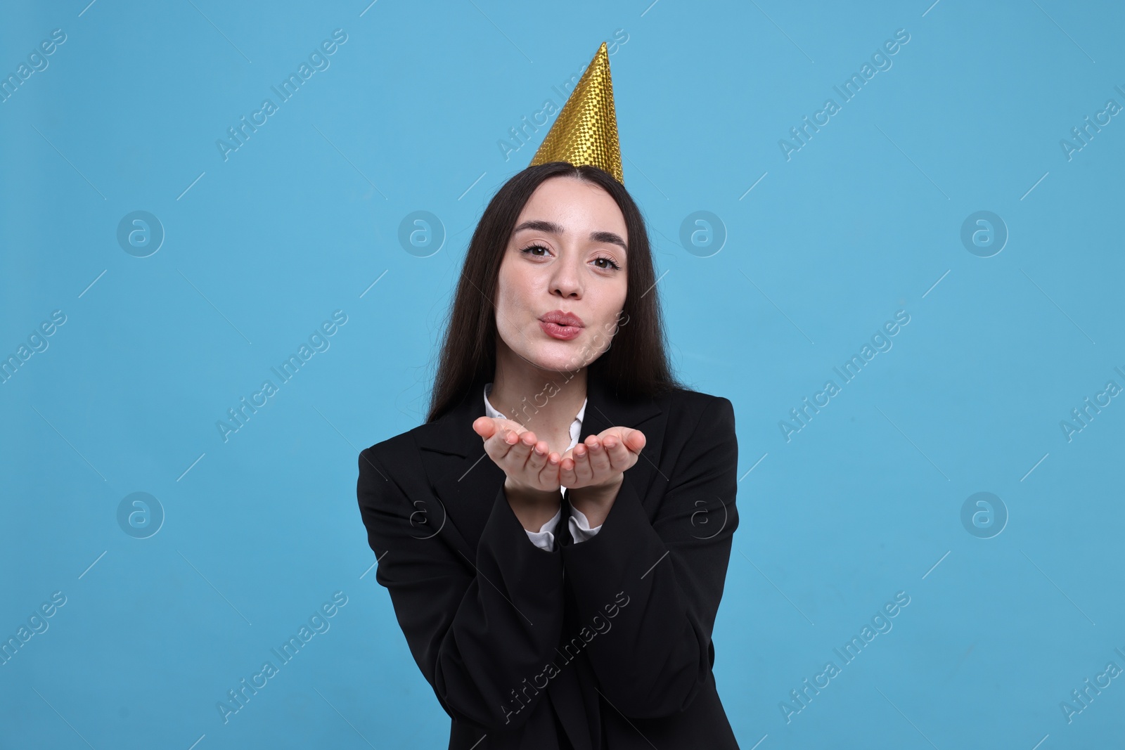 Photo of Happy woman in party hat blowing kiss on light blue background