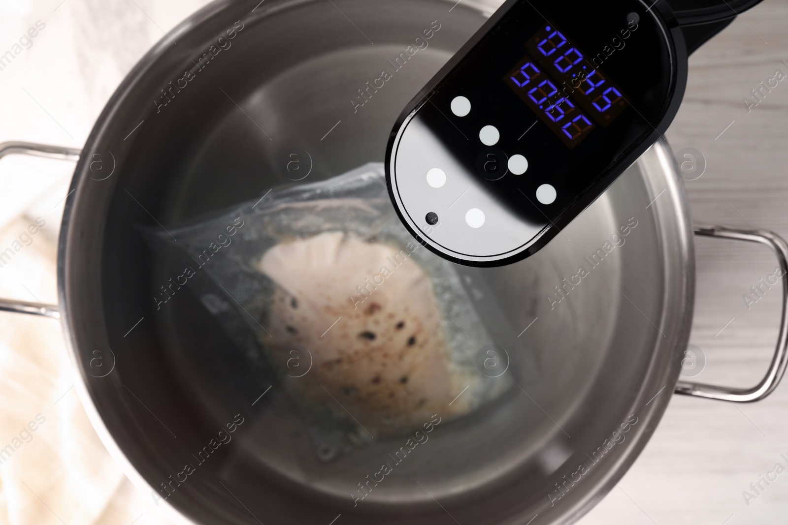 Photo of Thermal immersion circulator and vacuum packed meat in pot on white wooden table, top view. Sous vide cooking