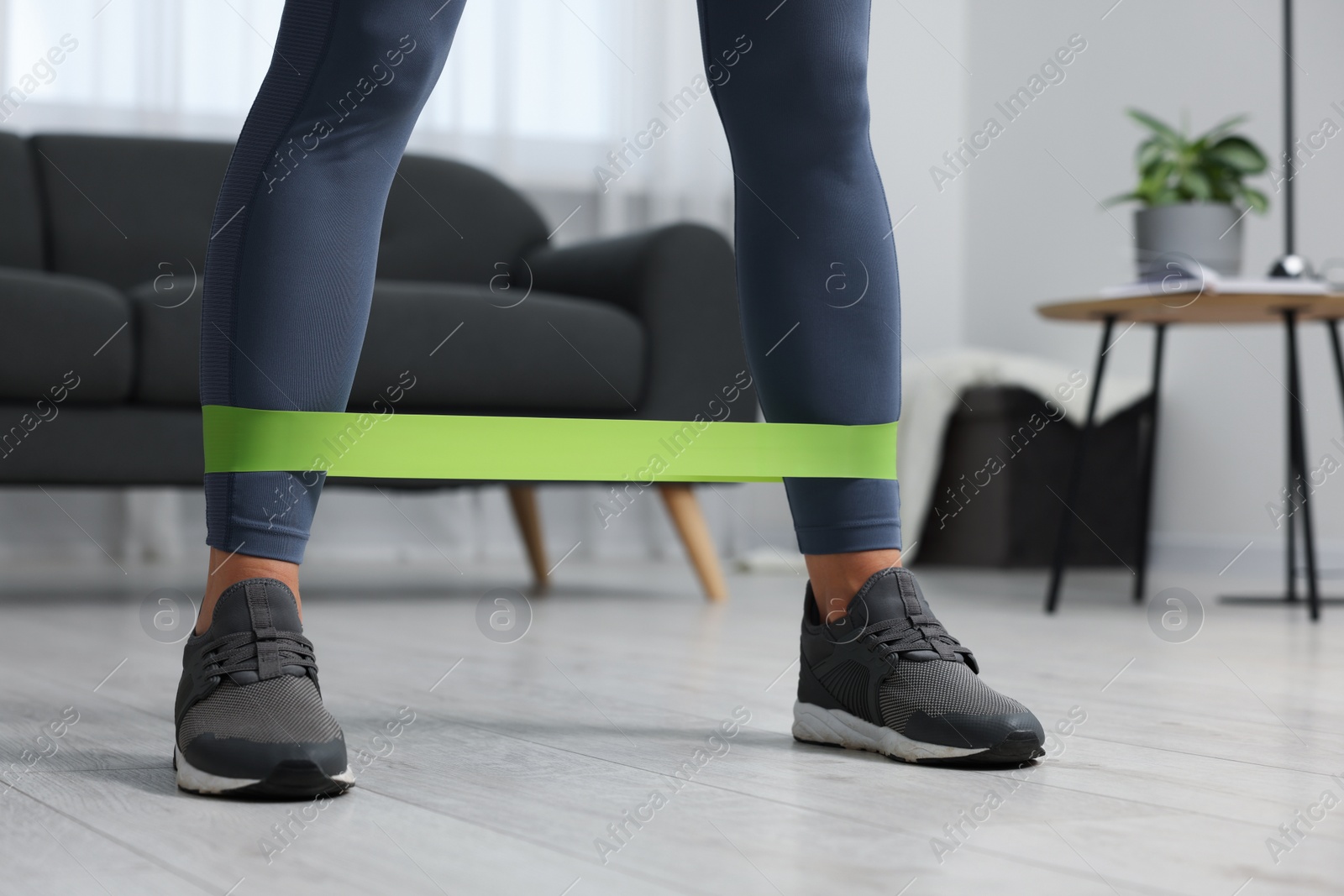 Photo of Woman doing exercise with fitness elastic band at home, closeup