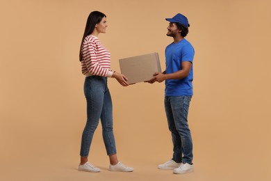 Photo of Smiling courier giving parcel to receiver on light brown background