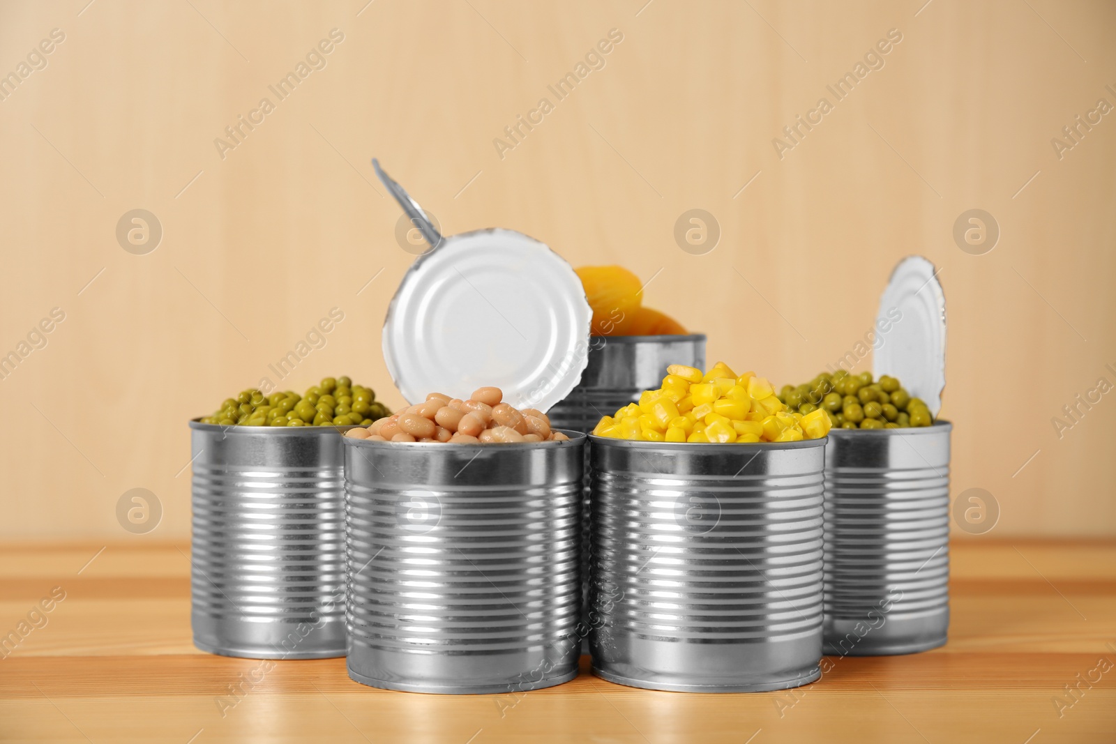 Photo of Open tin cans with conserved vegetables and fruits on wooden table