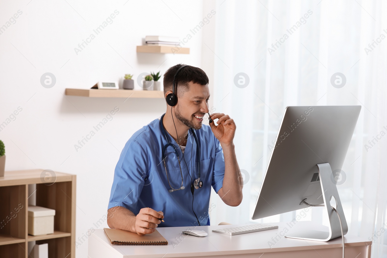 Photo of Doctor with headset consulting patient online at desk in clinic. Health service hotline