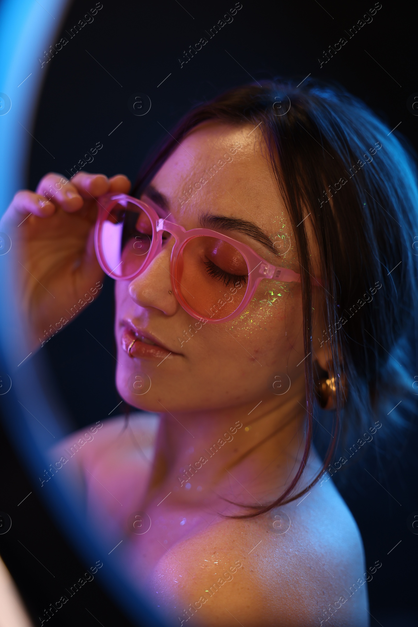 Photo of Beautiful woman in glasses on dark background in neon lights, view through ring lamp