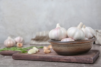 Photo of Bowl with ripe garlic bulbs on wooden board