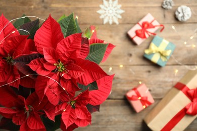 Photo of Poinsettia (traditional Christmas flower) and holiday items on wooden table, top view. Space for text