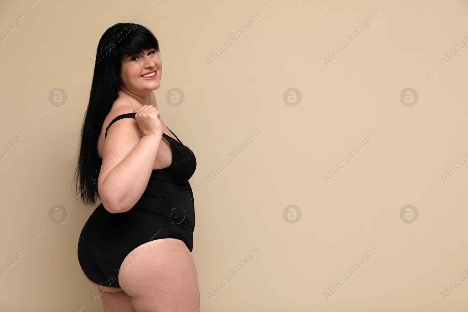 Photo of Beautiful overweight woman in black underwear on beige background, space for text. Plus-size model