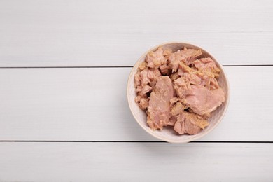 Photo of Bowl with canned tuna on white wooden table, top view. Space for text