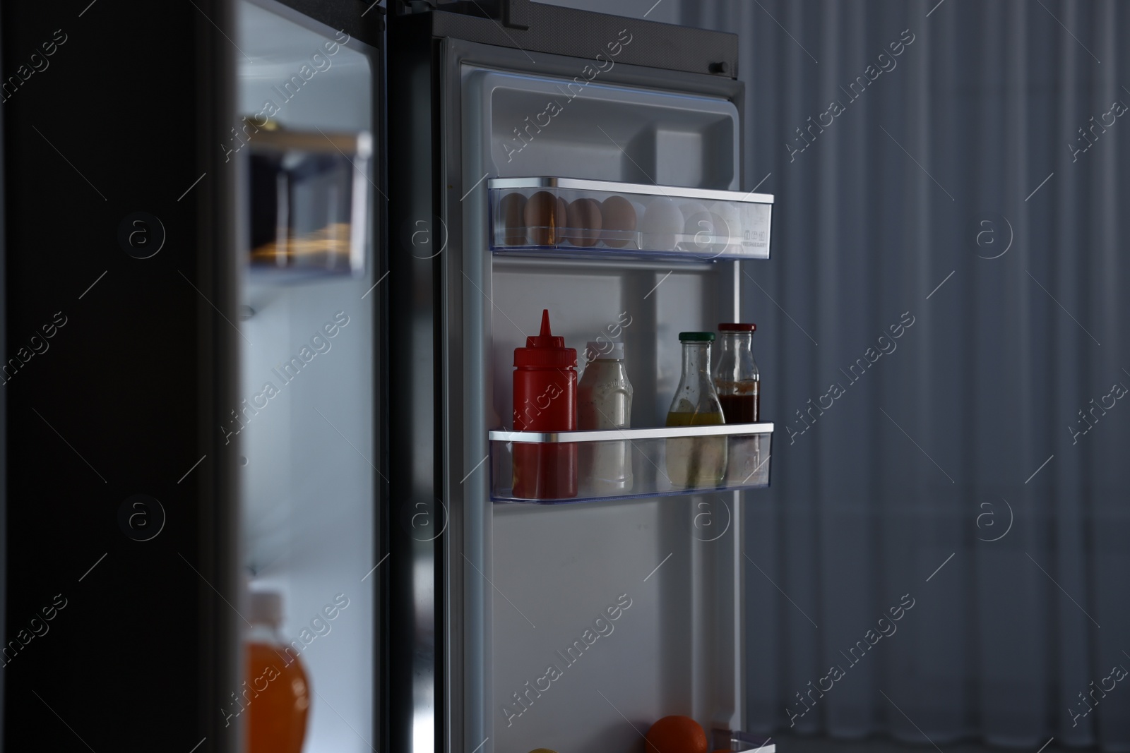 Photo of Open refrigerator full of different products indoors at night