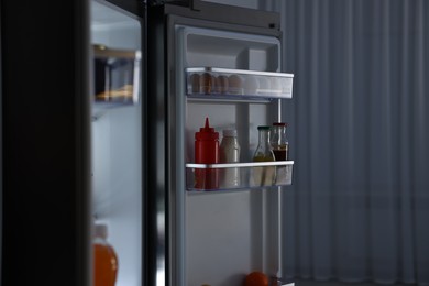 Photo of Open refrigerator full of different products indoors at night