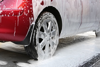 Red automobile covered with foam at car wash, closeup