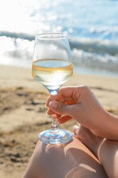 Woman with glass of tasty wine near sea, closeup