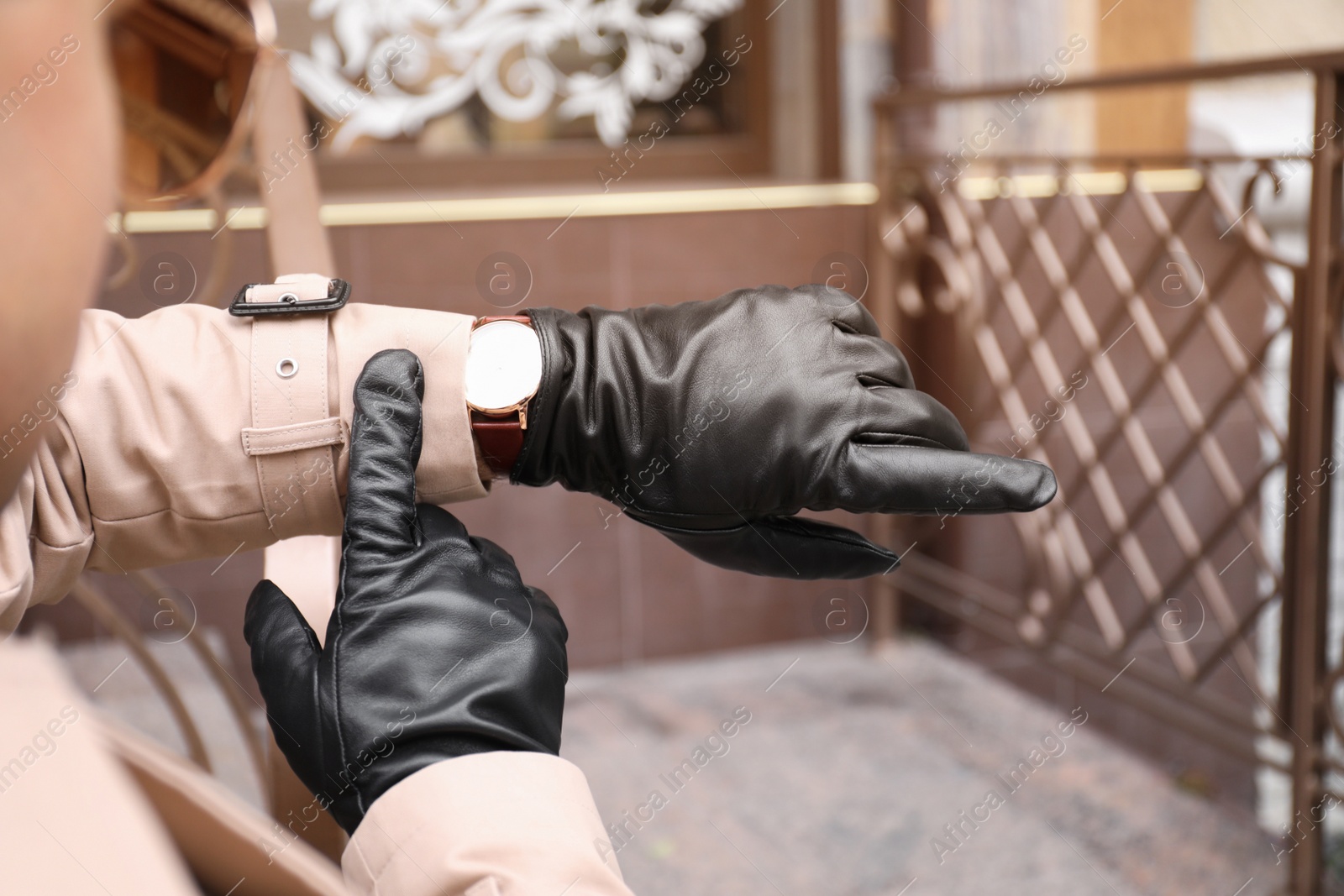 Photo of Stylish man in black leather gloves looking at his watch outdoors, closeup