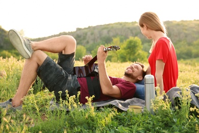 Photo of Man playing guitar for his girlfriend in wilderness. Camping season