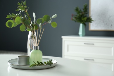 Photo of Eucalyptus branches, candle and aromatic reed air freshener on white table indoors, space for text. Interior elements