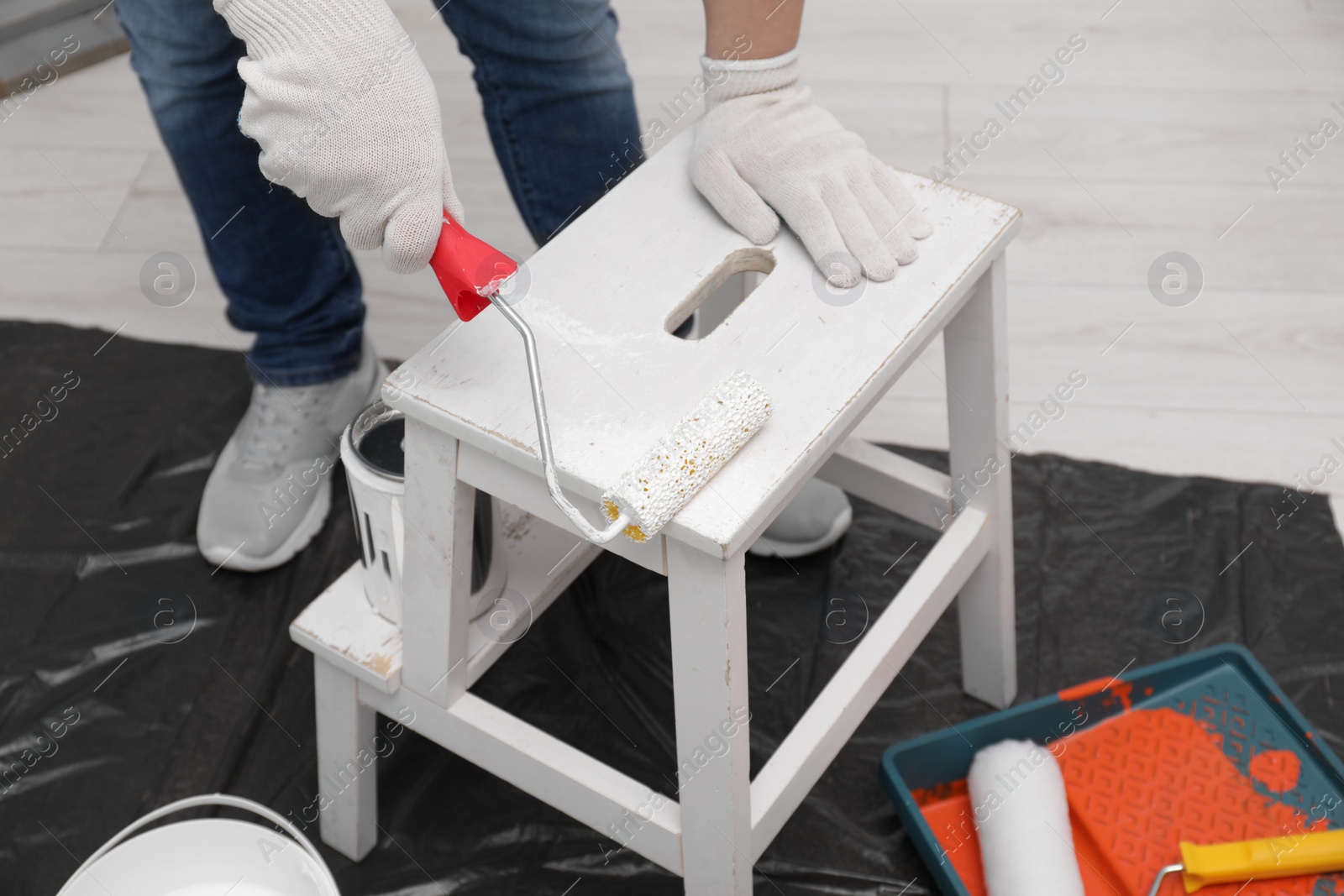 Photo of Man using roller to paint bekvam with white dye indoors, closeup