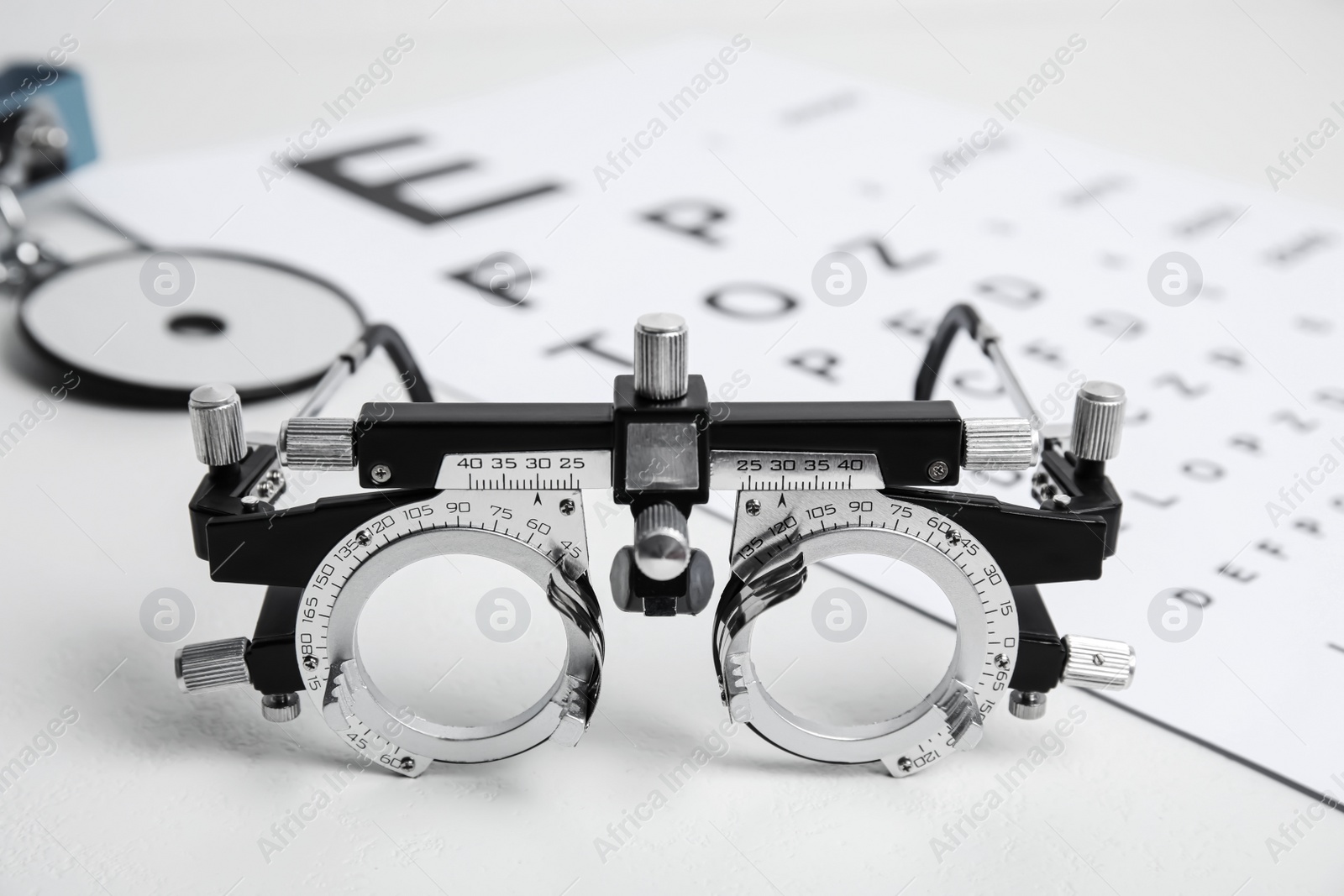 Photo of Trial frame, head mirror and eye chart test on white table. Ophthalmologist equipment