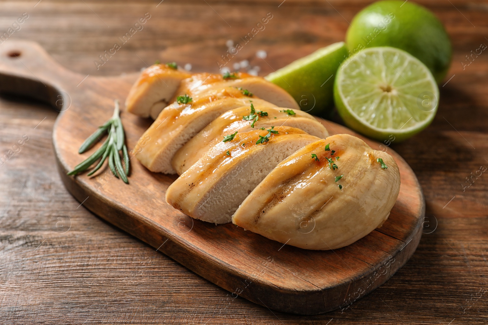 Photo of Wooden board with fried chicken breast and limes on table, closeup