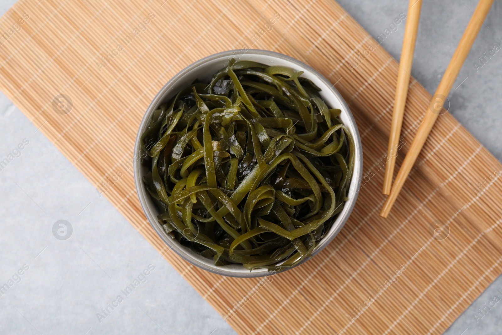 Photo of Tasty seaweed salad in bowl served on gray table, flat lay