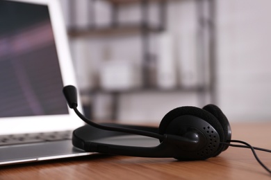 Photo of Modern laptop with headset on wooden table in office, closeup. Hotline service