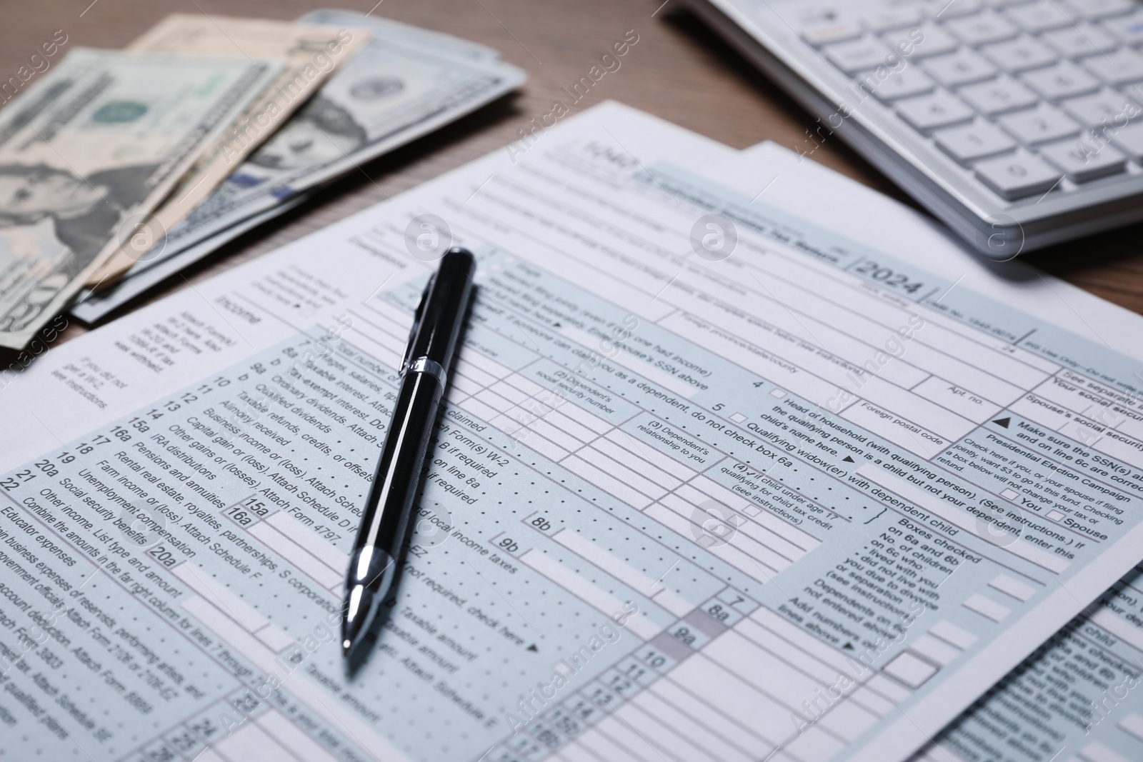 Photo of Payroll. Tax return forms, pen, dollar banknotes and calculator on table, selective focus