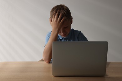 Photo of Upset boy with laptop at table, space for text. Cyber bullying