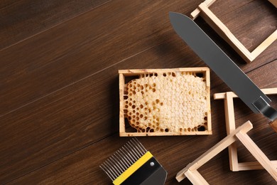 Photo of Honeycomb frames and beekeeping tools on wooden table, flat lay. Space for text