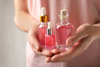 Photo of Woman holding bottles of rose essential oil in hands, closeup
