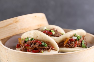 Photo of Delicious gua bao (pork belly buns) in bamboo steamer on grey background, closeup