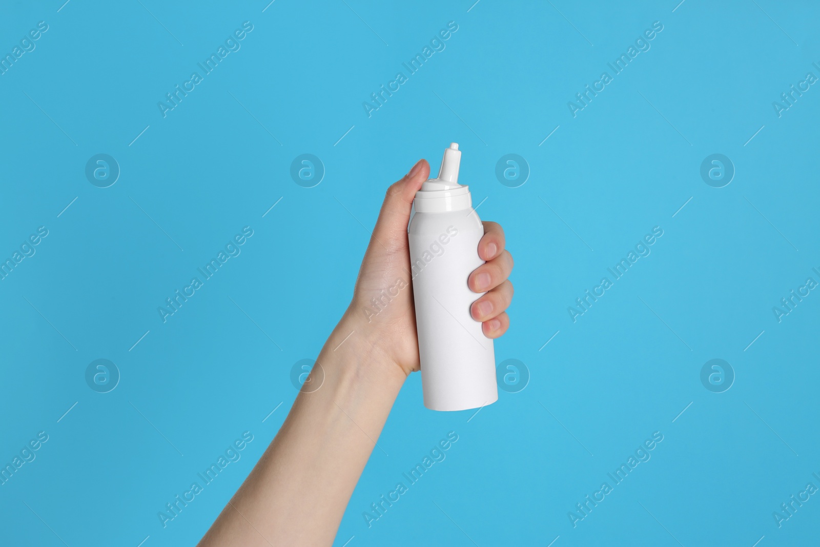 Photo of Woman holding nasal spray on light blue background, closeup