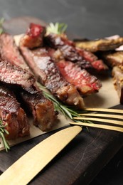 Photo of Delicious grilled beef with rosemary served on wooden board, closeup