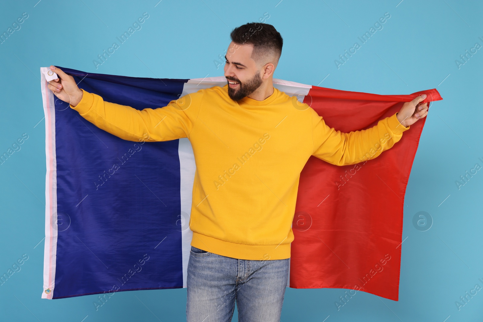 Photo of Young man holding flag of France on light blue background