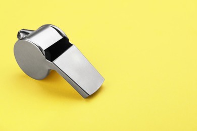 One metal whistle on yellow background, closeup and space for text